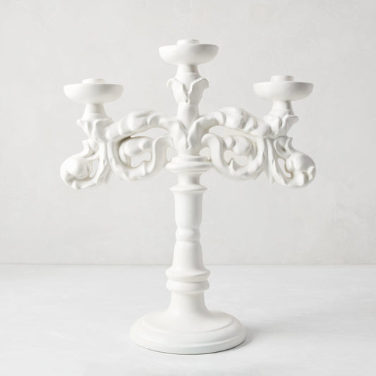 Baroque matte white ceramic candelabra, 18"H, with three candle holders and ornate scrollwork.