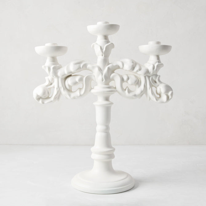 Baroque matte white ceramic candelabra, 18"H, with three candle holders and ornate scrollwork.