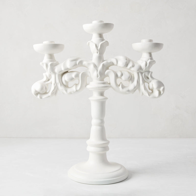 Baroque matte white ceramic candelabra, 18"H, with three candle holders and ornate scrollwork.