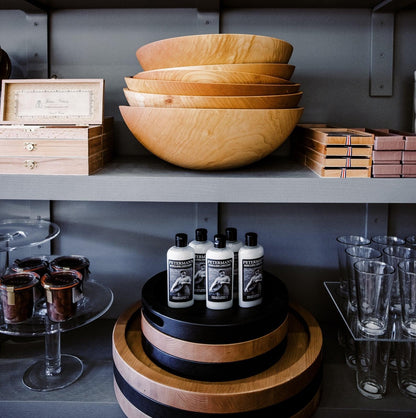 Peterman's Beeswax Conditioner bottles on a black stand, with wooden bowls and other products on shelves.