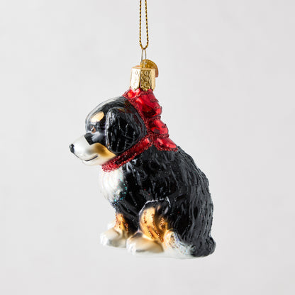 Hand-painted glass Bernadoodle dog ornament with a red glitter collar, hanging from a gold cord.