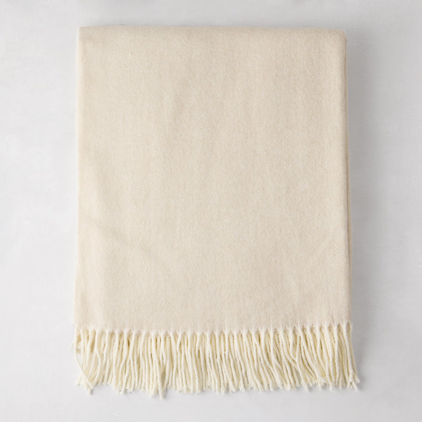 Birch off-white Italian herringbone throw blanket, folded, with fringe.