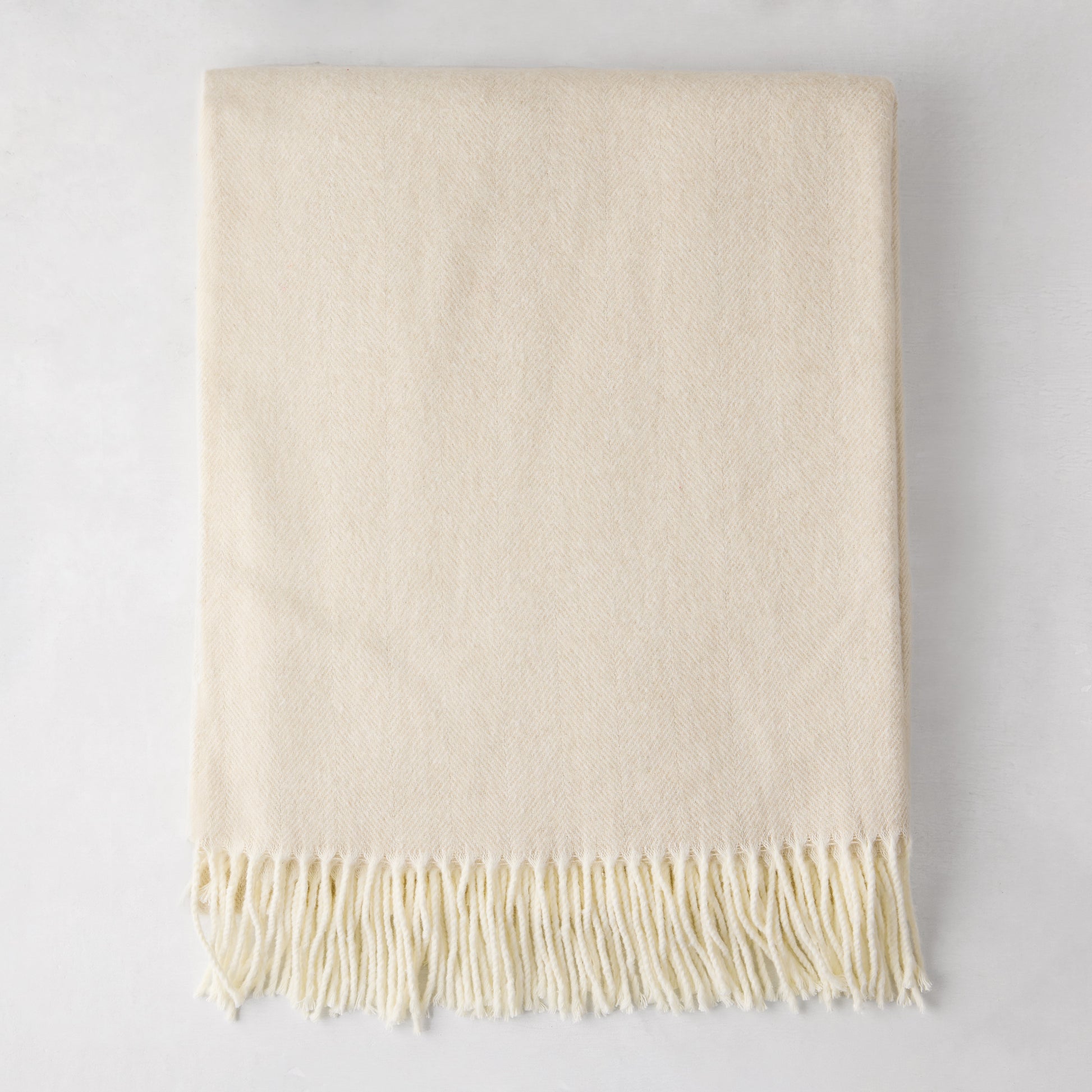 Birch off-white Italian herringbone throw blanket, folded, with fringe.