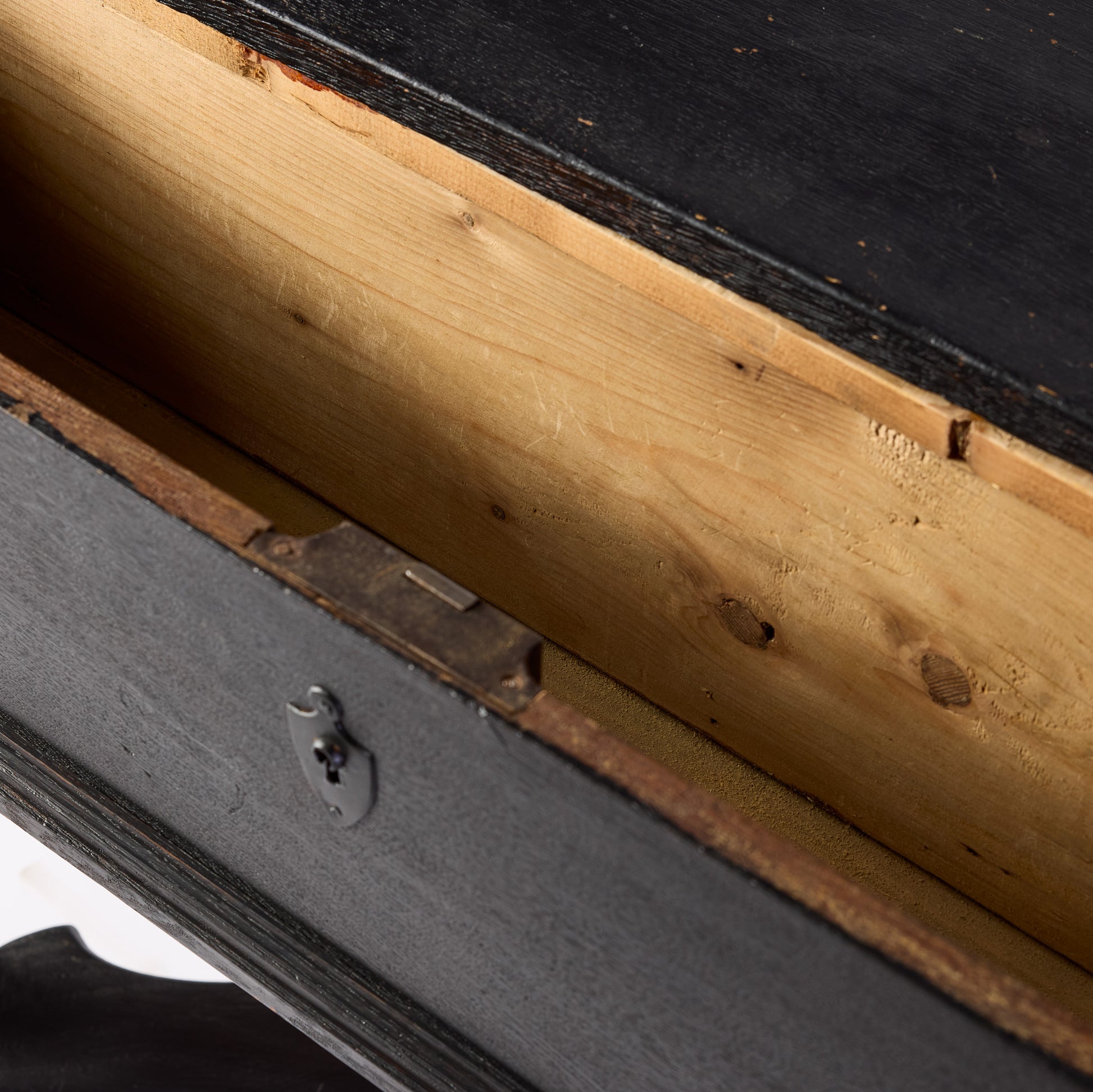 Open drawer of a black ebonized wood console table with a metal keyhole plate and natural wood interior.
