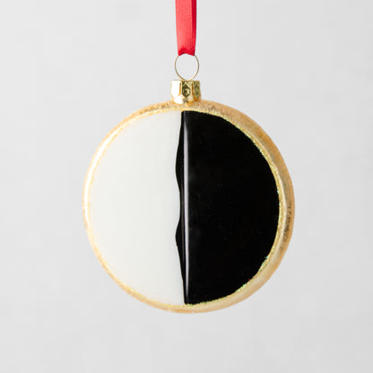 3.5-inch round black and white cookie Christmas ornament made of glass and resin with a red hanging ribbon.
