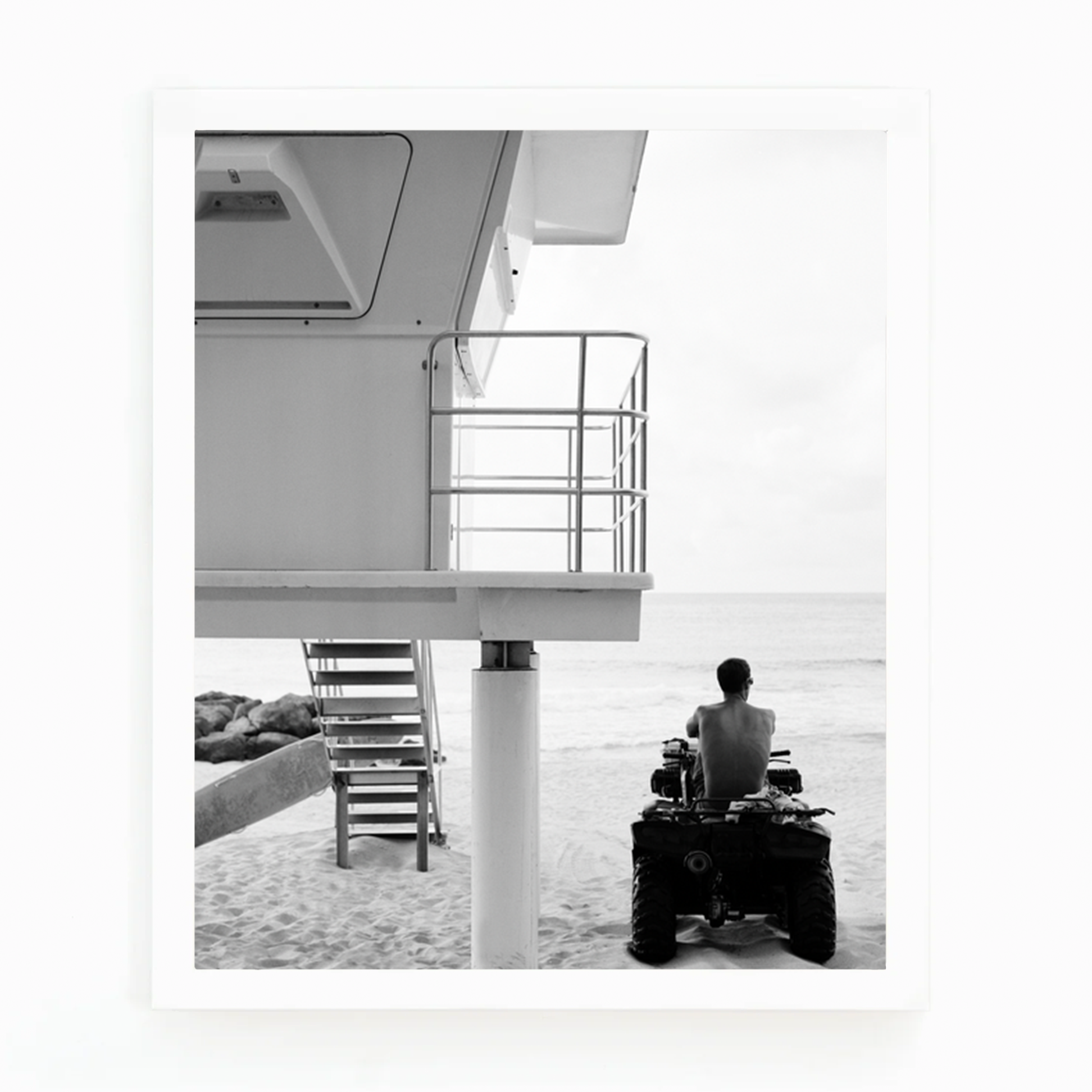 Black and white photograph by Matt Albiani of a lifeguard on an ATV next to a tower on a sandy beach.