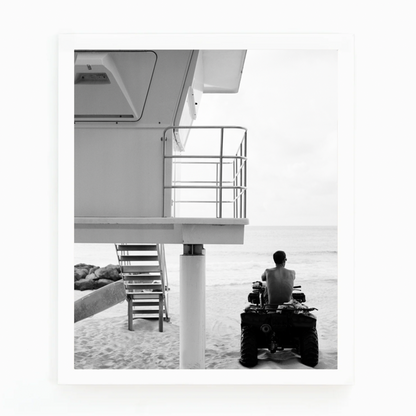 Black and white photograph by Matt Albiani of a lifeguard on an ATV next to a tower on a sandy beach.