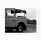Black and white photograph of a vintage surf truck with a soft top, parked on a road near dunes.