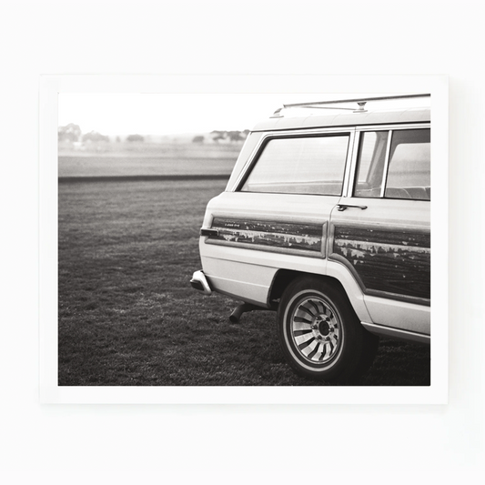 Black and white photograph of a vintage Wagoneer parked in a grassy field by Matt Albiani.