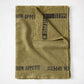 Folded green linen table runner with "BON APPETIT" in black text.