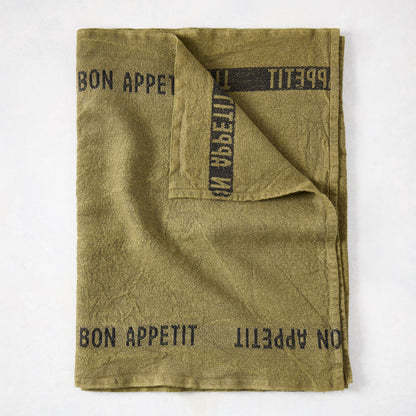 Folded green linen table runner with "BON APPETIT" in black text.