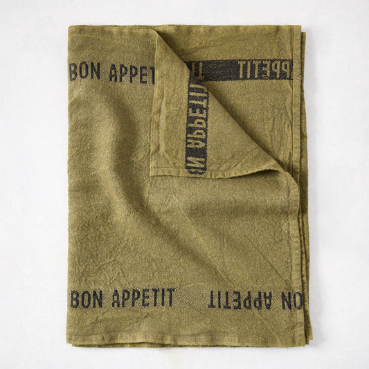 Folded green linen table runner with "BON APPETIT" in black text.