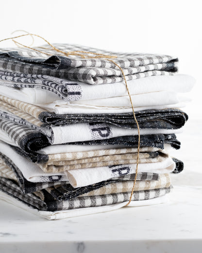 Stack of black, white, and beige linen hand towels with plaid and striped patterns, tied with twine.