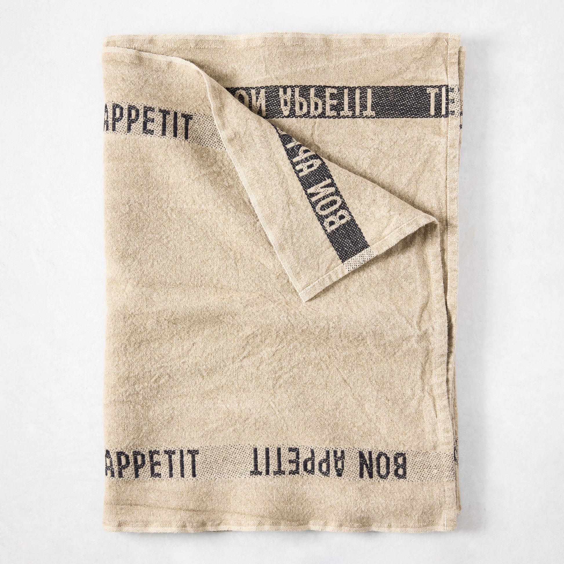 Khaki linen table runner with "Bon Appetit" printed in black, folded on a white surface.