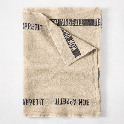 Khaki linen table runner with "Bon Appetit" printed in black, folded on a white surface.