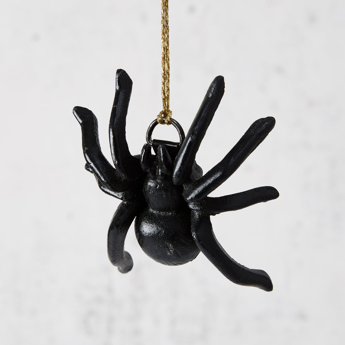 Black cast iron decorative spider, 3"L x 3.5"W, hanging by a gold string.