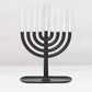Black cast iron Hanukkah menorah, 11"L x 11"H, with white taper candles and a tray-like base.
