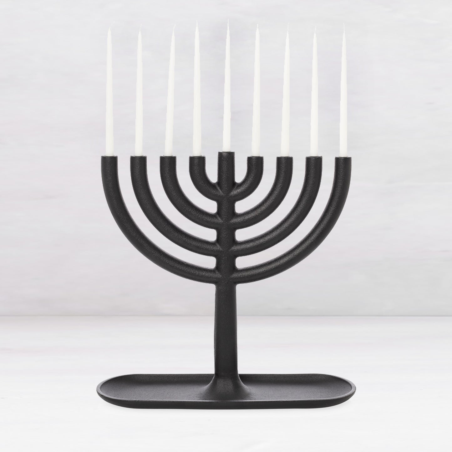 Black cast iron Hanukkah menorah, 11"L x 11"H, with white taper candles and a tray-like base.