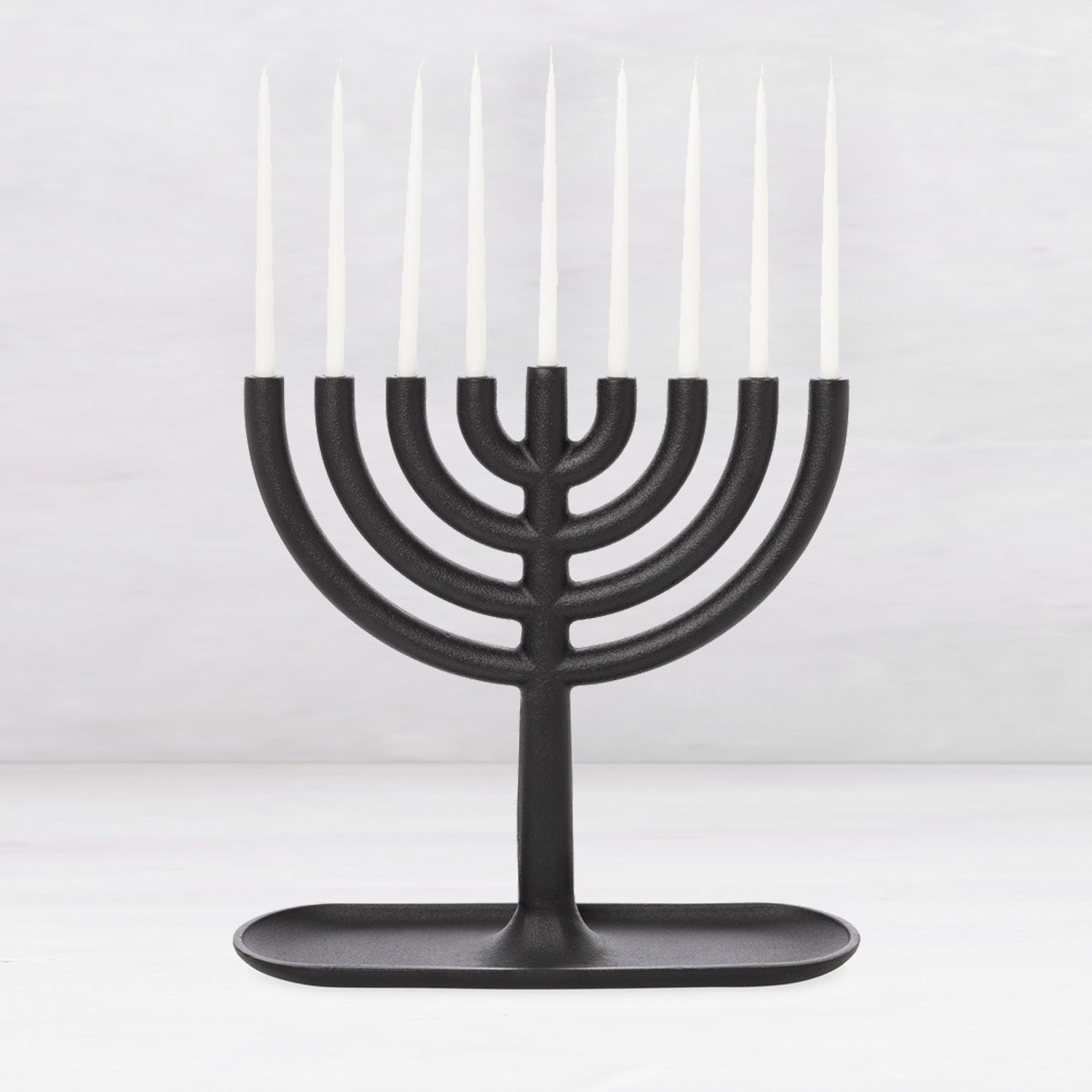 Black cast iron Hanukkah menorah, 11"L x 11"H, with white taper candles and a tray-like base.