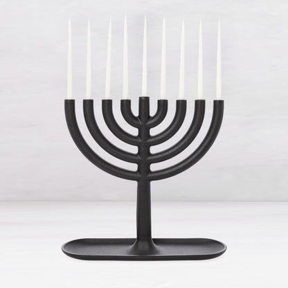 Black cast iron Hanukkah menorah, 11"L x 11"H, with white taper candles and a tray-like base.