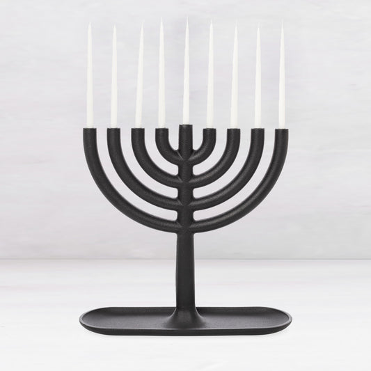 Black cast iron Hanukkah menorah, 11"L x 11"H, with white taper candles and a tray-like base.