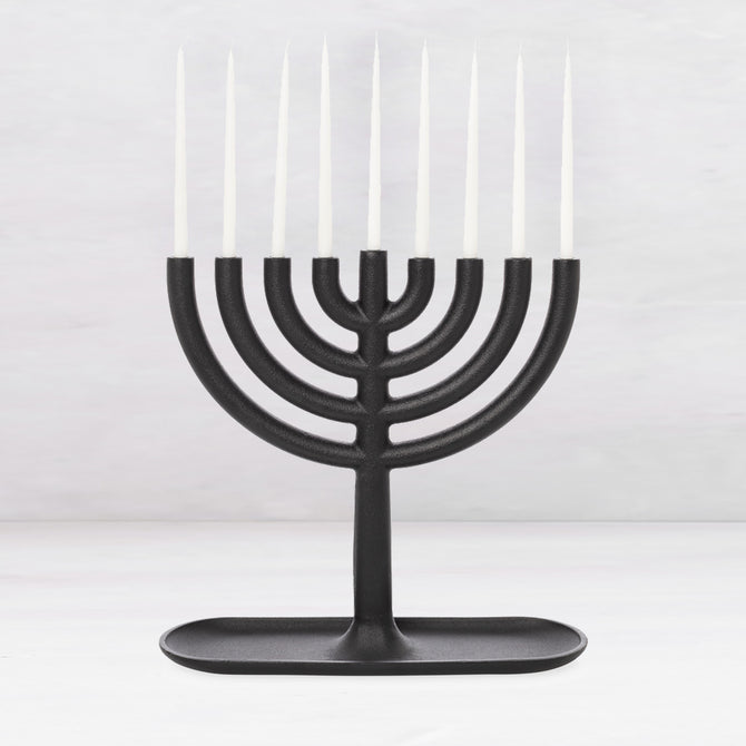 Black cast iron Hanukkah menorah, 11"L x 11"H, with white taper candles and a tray-like base.