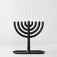 Modern black cast iron Hanukkah menorah by Josh Owen with a tray base and nine thin white taper candles.