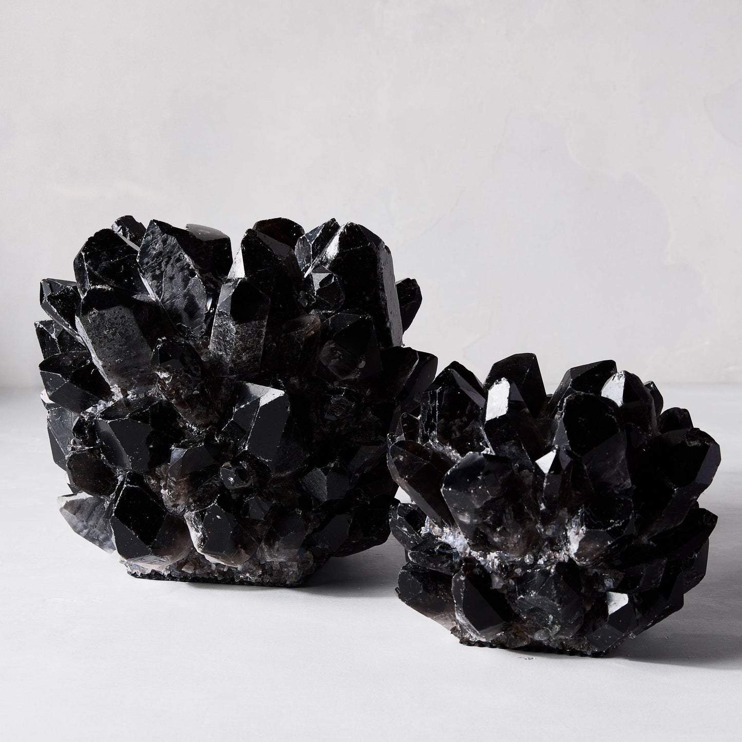 Two black genuine quartz crystal votive candle holders, one larger, one smaller, on a white surface.
