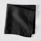 Black HG Signature hand-dyed 22-inch linen napkin, folded on a light surface.