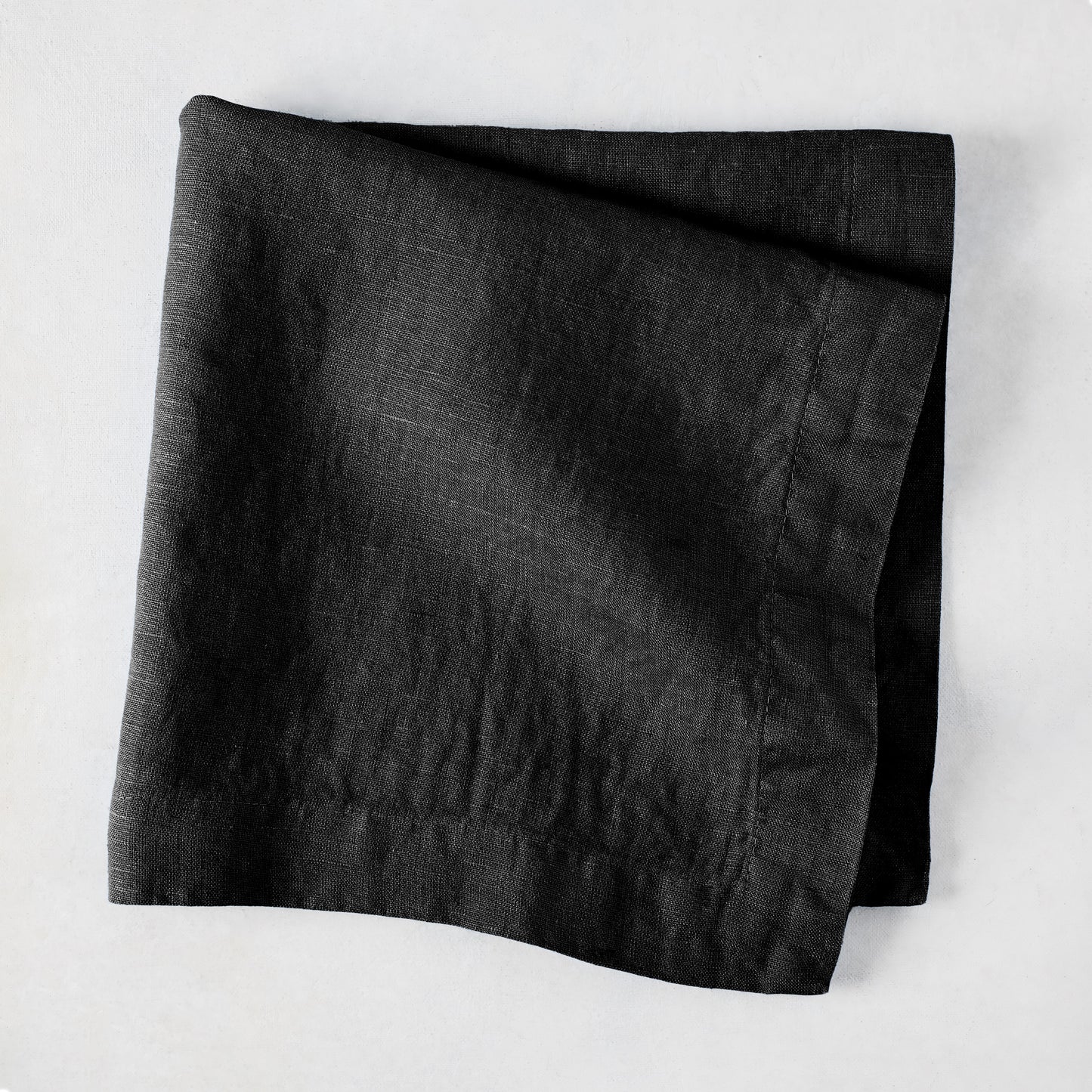 Black HG Signature hand-dyed 22-inch linen napkin, folded on a light surface.