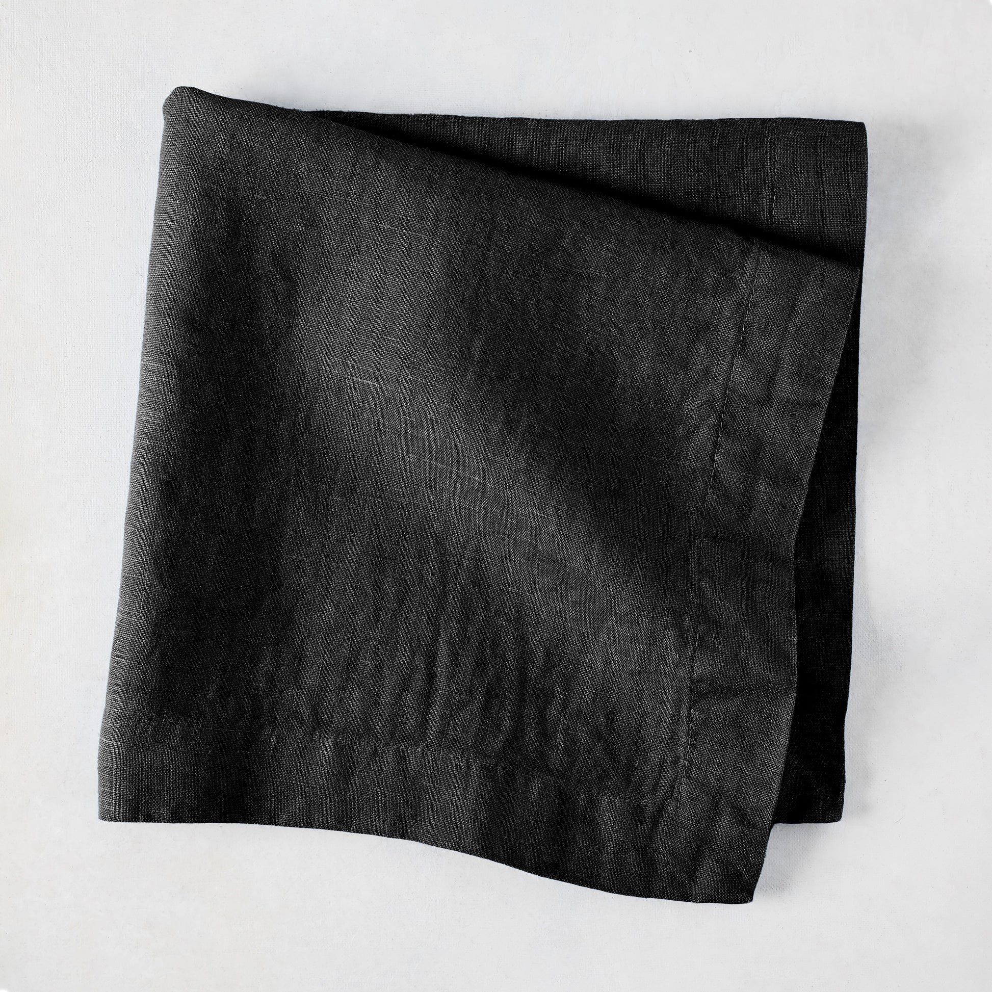 Black HG Signature hand-dyed 22-inch linen napkin, folded on a light surface.
