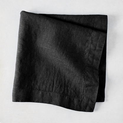 Black HG Signature hand-dyed 22-inch linen napkin, folded on a light surface.