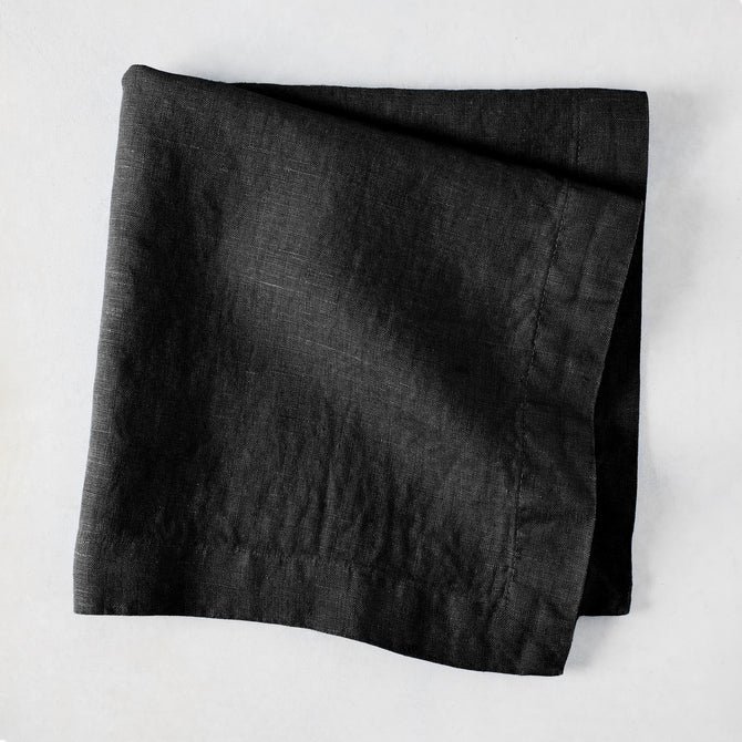 Black HG Signature hand-dyed 22-inch linen napkin, folded on a light surface.