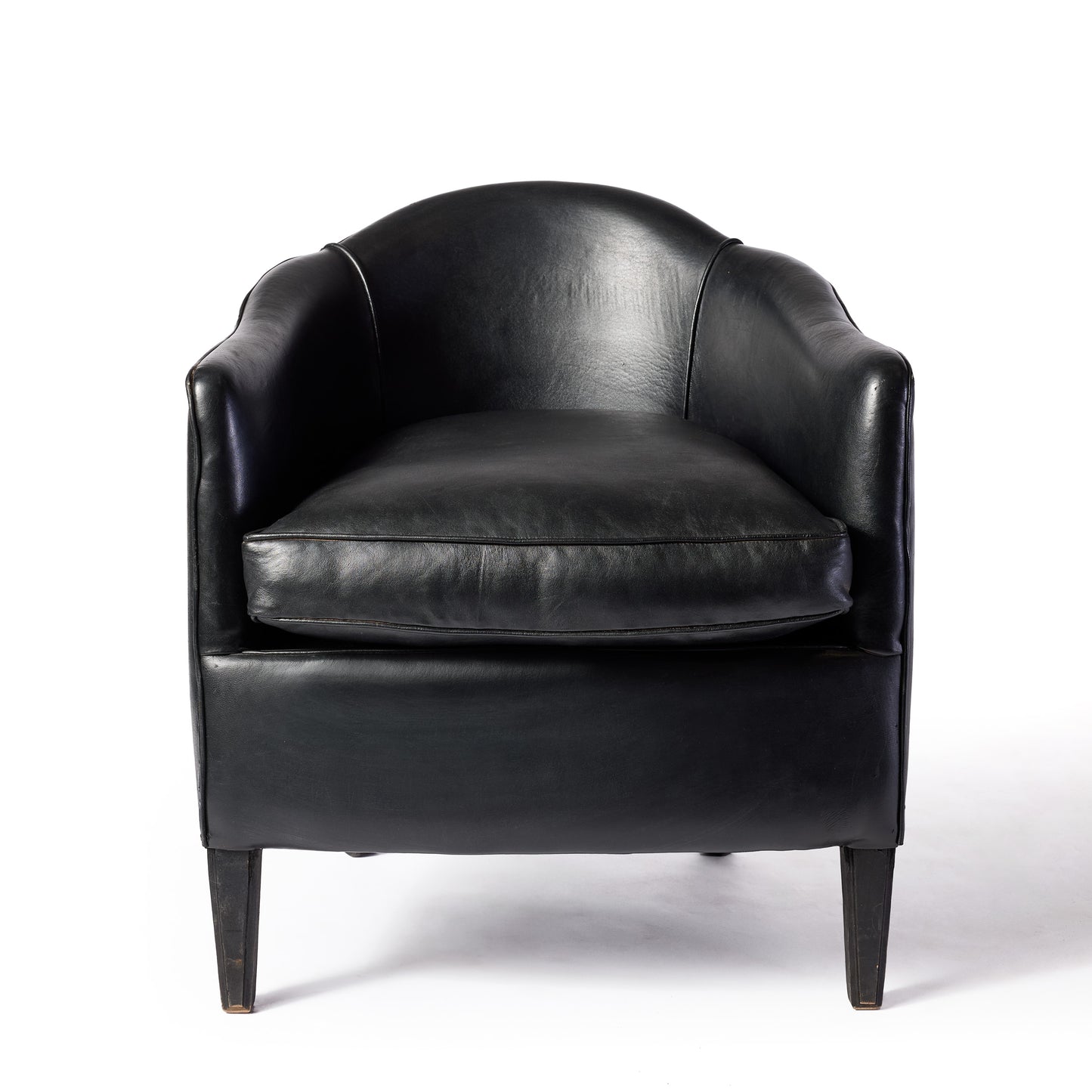 Vintage black leather club armchair with a scalloped arched back and sleek ebonized wood legs.