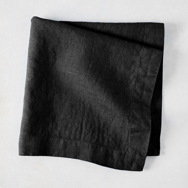 Black HG Signature hand-dyed 22-inch linen napkin, folded on a light surface.