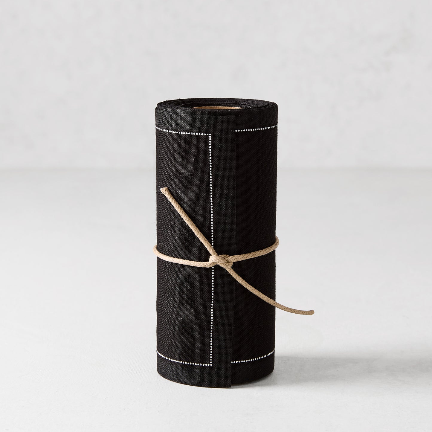 Black cotton cocktail napkin roll with white dotted border, tied with twine.