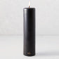 3x12 inch black unscented pillar candle with a gold HG logo and a lit cotton wick.