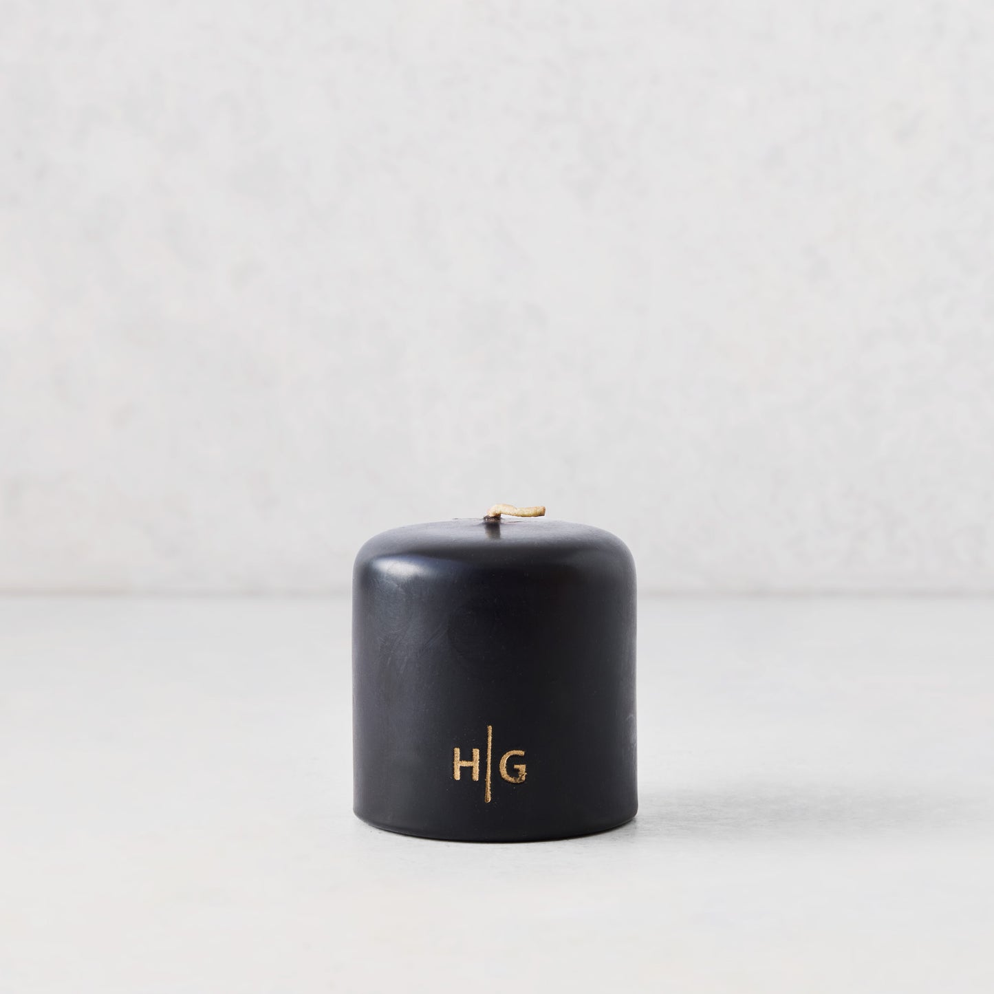 3x3 inch black unscented pillar candle with gold HG logo, hand-dipped paraffin and amber resin.