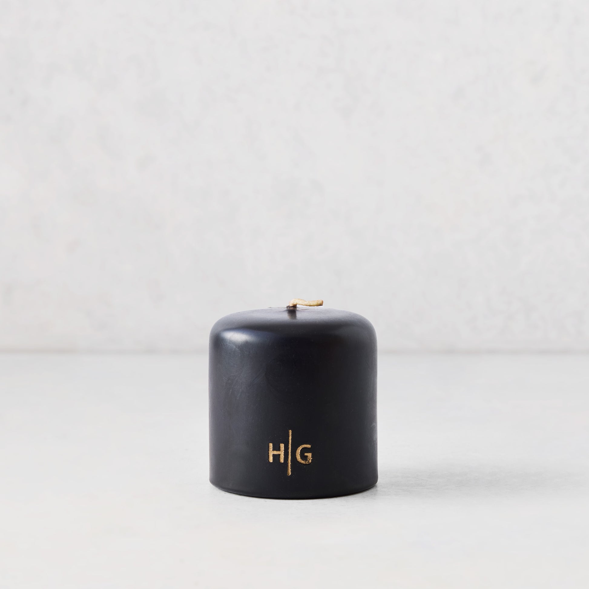 3x3 inch black unscented pillar candle with gold HG logo, hand-dipped paraffin and amber resin.