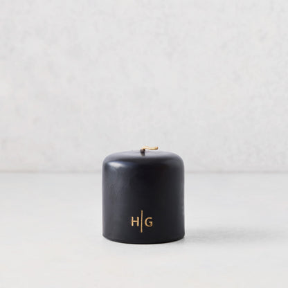 3x3 inch black unscented pillar candle with gold HG logo, hand-dipped paraffin and amber resin.