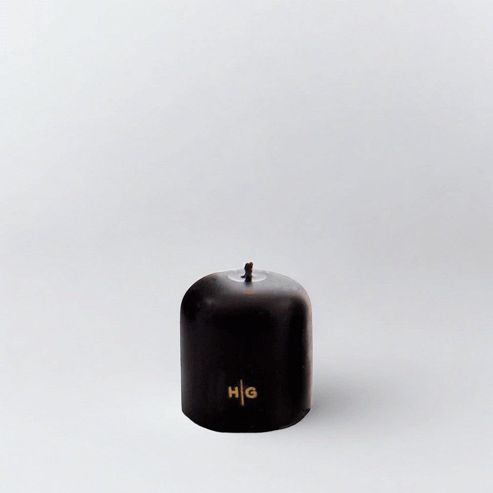 HG Black 3"x3" unscented pillar candle with gold embossed HG logo and oversized cotton wick.
