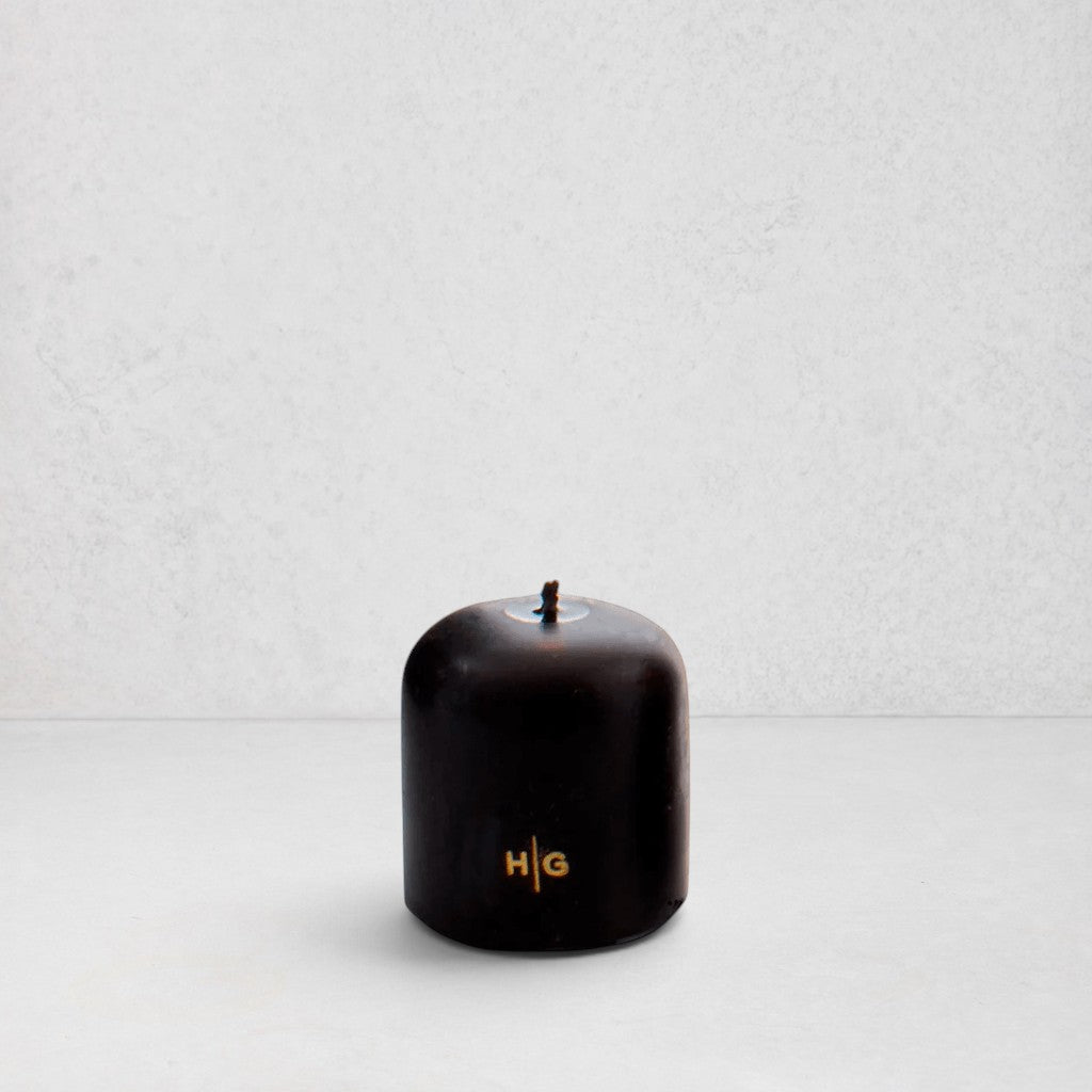 Hudson Grace black unscented pillar candle with gold HG logo and oversized cotton wick on a white background