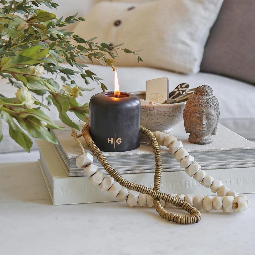 HG Black Unscented Pillar Candle, 3"x4", with gold HG logo, burning on books with decor.