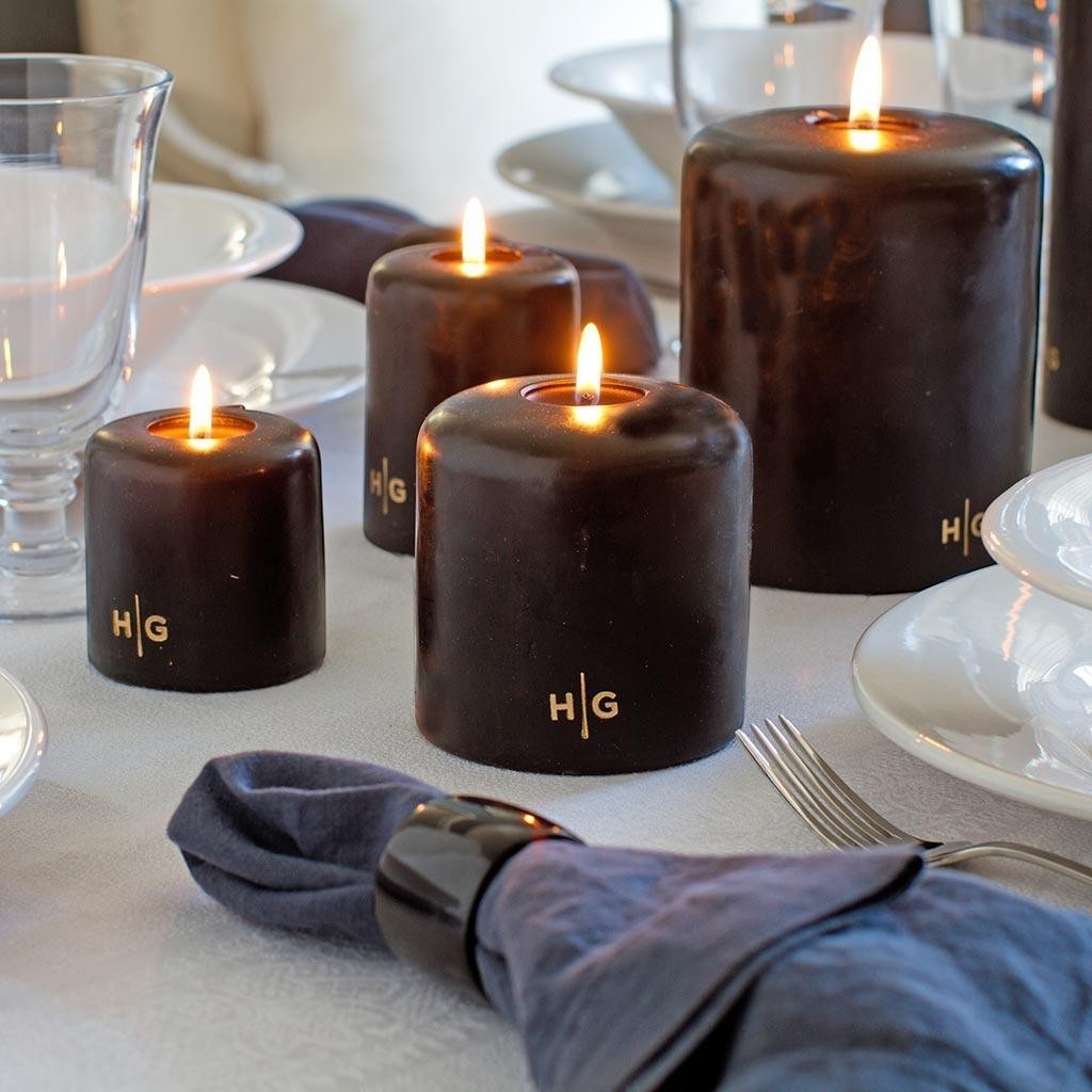 HG Black unscented pillar candles, 3"x4", with gold HG logo, lit on a dining table.