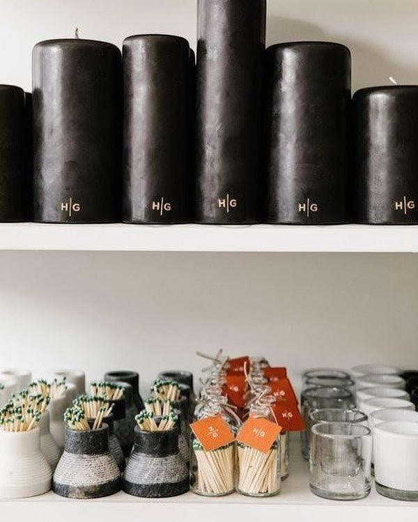 HG Black 3"x4" unscented pillar candles with gold HG logo, displayed above matches and votives.