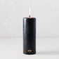 3x8 inch black unscented pillar candle with a gold HG logo and lit cotton wick.