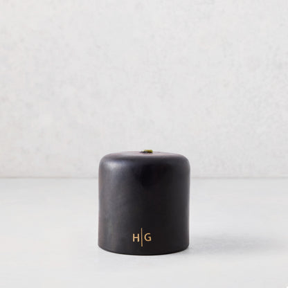 4"x4" black unscented pillar candle with gold HG logo, hand-dipped paraffin and amber resin.