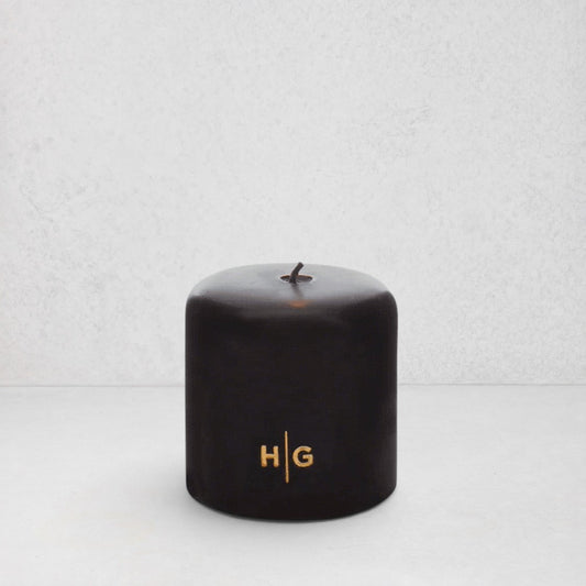 HG Black Unscented Pillar Candle, 4"x4", with gold embossed HG logo and oversized cotton wick.