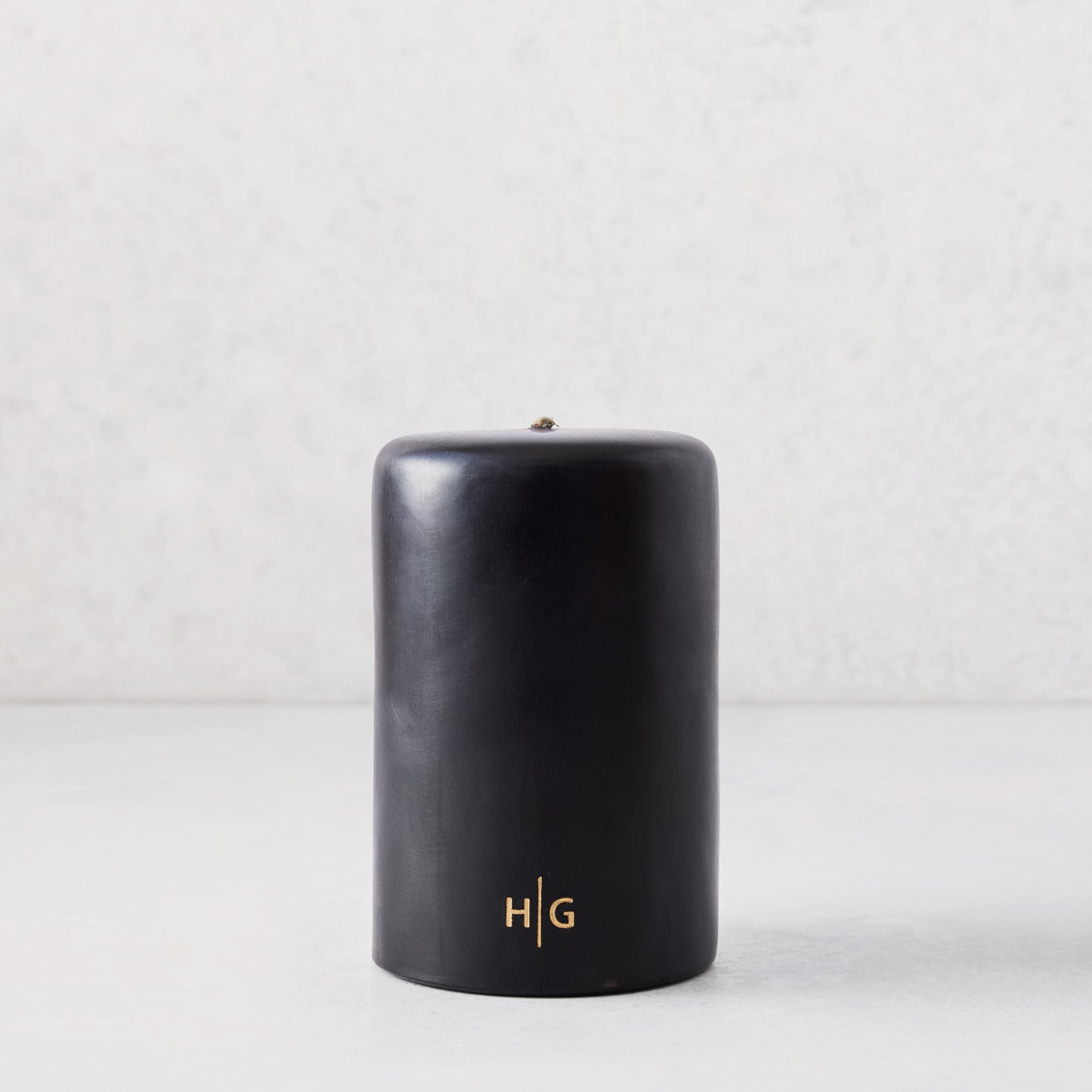4x6 inch black hand-dipped pillar candle with a gold HG logo, made from paraffin and amber resin.