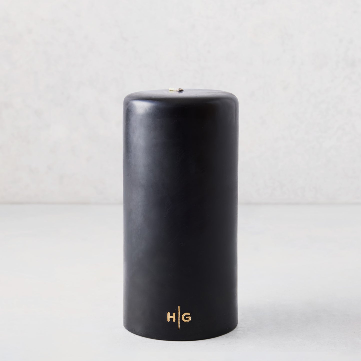 4x8 inch black hand-dipped pillar candle with gold HG logo and cotton wick.